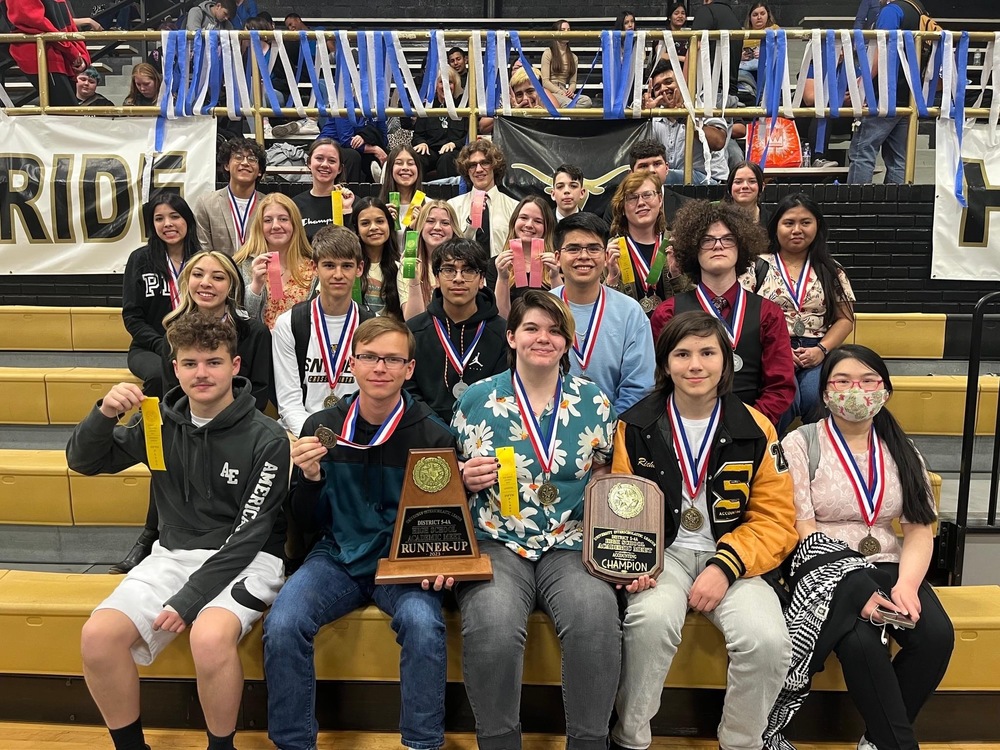 group of students smile holding medals, ribbons, and plaques at UIL competition