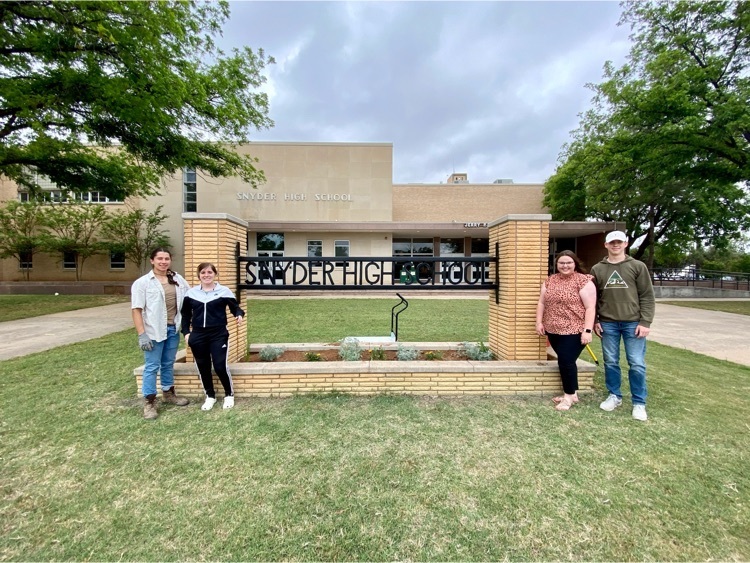 students posing in front of new sign and flowers