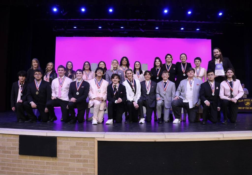 group of theatre students wearing pink and black attire pose on stage for photo